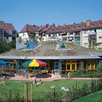 Ein strahlender Tag enthüllt die moderne Eleganz des Kindergartens Luisenstrasse in Nürnberg, umgeben von grünen Spielbereichen, die die natürliche Umgebung perfekt ergänzen. - SÄBU Holzbau