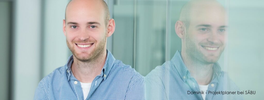 Dominik ist Projektplaner bei SÄBU Holzbau im Allgäu. Ein charismatischer, lächelnder Mann in seinem Büro mit einem blauen Karo-Hemd. Er vertritt das Gesicht von SÄBU für ein offenes Stellenangebot in der Projektplanung.